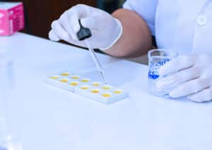 Hand's Scientist or Researcher wear latex gloves using a dropper to drop red chemicals from beaker into white plate in laboratory Science